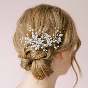 May include: A silver and white floral hair comb with pearl accents. The comb is designed to be worn in the hair for a wedding or special occasion.