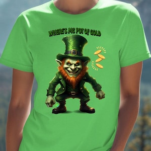May include: A lime green t-shirt featuring a cartoon leprechaun with a green hat and jacket, and the text "WHERE'S ME POT OF GOLD". The design includes gold coins. The shirt is worn by a person in front of a mountain backdrop.
