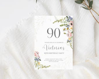 Peut inclure: Une invitation blanche pour un 90e anniversaire avec des motifs floraux. L'invitation présente le chiffre "90" en gris, le nom "Victoria's" et les détails de l'événement. Des arrangements floraux roses, blancs et bleus ornent les coins.