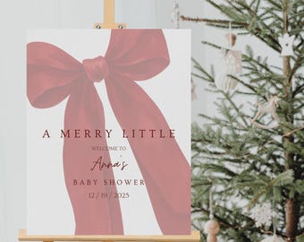 May include: A baby shower welcome sign on an easel. The sign features a large burgundy bow graphic and the text "A Merry Little" above "Welcome to Anna's Baby Shower 12/19/2025". The easel is made of wood.