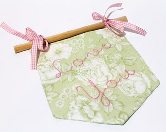 Puede incluir: Una pancarta de tela verde con un patrón floral y bordado rosa que dice "Love You". La pancarta está unida a una varilla de madera con una cinta de cuadros rosa.