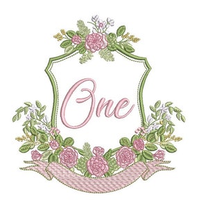 May include: Embroidered design featuring a green shield with a pink banner and the word "One" in pink script. The shield is surrounded by a wreath of green leaves and pink roses.