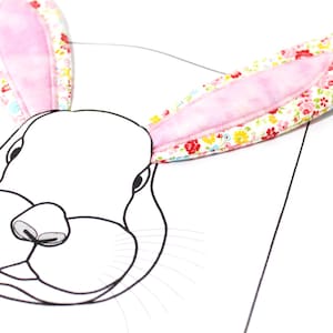 Peut inclure: Un contour blanc d'un visage de lapin avec des oreilles de lapin en tissu rose et floral. Les oreilles sont cousues ensemble et ont une doublure en tissu rose.