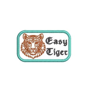 Puede incluir: Parche bordado con la cabeza de un tigre en tonos marrón y naranja, y el texto "Easy Tiger" en una fuente estilizada. El parche tiene un borde turquesa claro y un fondo blanco.