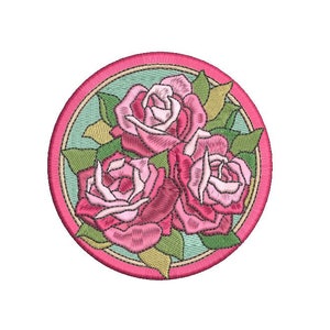 May include: Embroidered patch showing three pink roses with green leaves, set within a light blue and pink circular frame. The roses have detailed shading, and the leaves have a textured appearance. The patch is designed for sewing or ironing onto fabric.