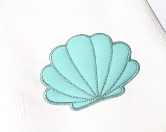 May include: A light blue embroidered seashell design on a white fabric background.
