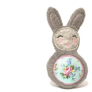 May include: A gray plush bunny toy with embroidered eyes and a smiling mouth. The bunny has a floral patterned fabric circle on its belly.