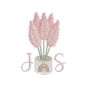 May include: An embroidery design featuring five light pink pampas grass stems in a cylindrical pot. The pot displays a small rainbow graphic on its front. The capital letters J and S are positioned on the left and right sides of the pot.