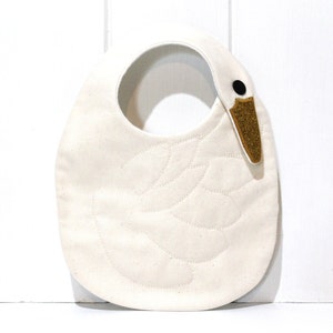 May include: A white swan-shaped baby bib with a brown felt beak and black eye.