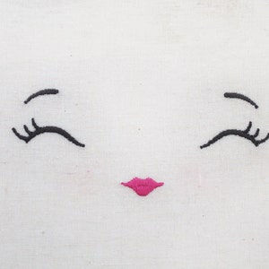 May include: Embroidered white fabric with a simple face design. The face has two black eyelashes and a pink smiling mouth.