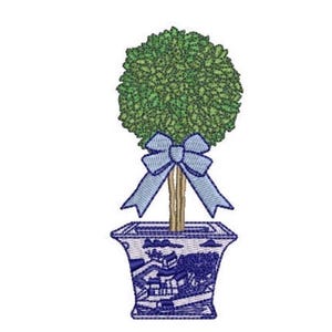 May include: An embroidery design of a topiary tree with a round green foliage ball, a brown trunk, and a light blue bow tied around the stem. The tree is planted in a square, blue and white patterned planter featuring a detailed landscape scene.