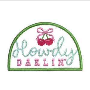 May include: A semi-circular embroidered patch with a white background and a green border. It features two red cherries with a pink bow on top. The text Howdy is embroidered in light blue script, and the word DARLIN' is in pink block letters.
