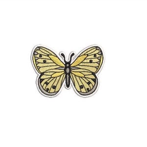 May include: An embroidered butterfly patch featuring pale yellow wings with dark grey vein detailing, black spots along the edges, and a central black body with two antennae, all outlined with a white border against a plain white background.