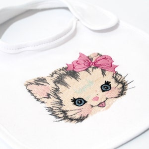 May include: White baby bib with an embroidered image of a kitten wearing a pink bow. The kitten has black eyes and a pink nose.