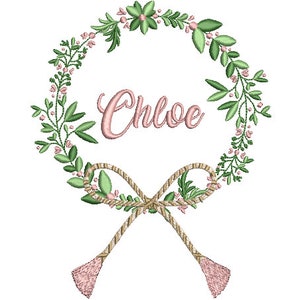 May include: An embroidery design featuring a circular wreath of green leaves and small pink flowers. The name Chloe is stitched in pink cursive script in the center. At the bottom, a tan rope-style bow with two dangling tassels completes the motif.
