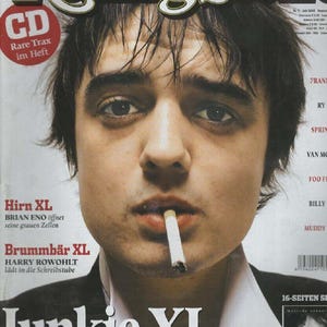 Könnte beinhalten: Ein Rolling Stone Magazin-Cover mit einem Porträt einer Person mit dunklem, zerzaustem Haar und einer Zigarette im Mund. Der Text umfasst Rolling Stone, CD Rare Trax im Heft, Hirn XL, Brummbar XL, Junkie XL und Pete Doherty.