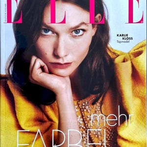 Może przedstawiać: Okładka magazynu ELLE z Karlie Kloss. Okładka ma duże różowe logo "ELLE" u góry z datą "KWIECIEŃ 2026". Modelka ma na sobie żółty top z ozdobami i widoczne są słowa "mehr FARBE!"