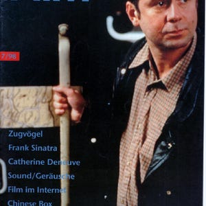 Könnte beinhalten: Ein Magazin-Cover mit dem Titel epd Film 7/98 zeigt einen Mann in einem beigen karierten Hemd und einer schwarzen Jacke. Der Text listet Artikel auf, darunter Zugvögel, Frank Sinatra, Catherine Deneuve, Sound/Geräusche, Film im Internet, Chinese Box, Der Geschmack der Kirsche sowie Interviews mit Bruno Ganz und Wayne Wang.