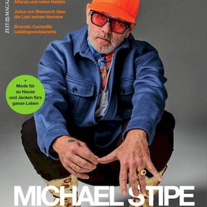 May include: Magazine cover featuring Michael Stipe, wearing an orange cap, glasses, and a blue jacket. The magazine title is "ZEIT MAGAZIN MANN." Text includes "Herbst - Winter 2021" and "MICHAEL STIPE."