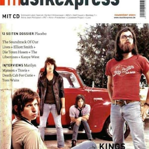 Puede incluir: Un número de noviembre de 2004 de la revista Musikexpress con una portada que muestra a cuatro personas frente a un camión rojo antiguo. La portada incluye texto como Musikexpress, 12 Seiten Dossier Placebo y Kings of Leon, Gottes Werk und Teufels Beitrag.