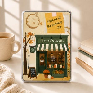 May include: A rectangular tablet case featuring an illustration of a green storefront with a striped awning, a tree with orange leaves, a coffee stain, and a yellow note that reads meet me at the bookshop -me. The shop window displays books.