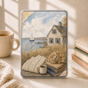 May include: A rectangular tablet case featuring a coastal landscape print of a house by the sea, a sailboat, tall grasses, a beige cable-knit sweater, a small speckled mug, and a stack of three vintage books with a bouquet of dried flowers on top.