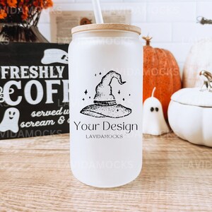 May include: White tumbler with a black and white witch hat design. The tumbler has a wooden lid and a straw. The tumbler is sitting on a wooden table with pumpkins and a ghost.
