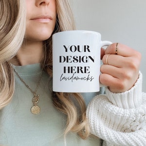 May include: White ceramic mug with black text that reads "YOUR DESIGN HERE lavidamocks". A woman is holding the mug with her right hand.