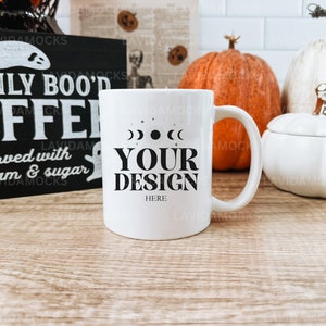 May include: White ceramic coffee mug with a black design of moons and the text "YOUR DESIGN HERE". The mug is on a wooden table with pumpkins and a sign that reads "FRESHLY BOO'D COFFEE served with scream & sugar".