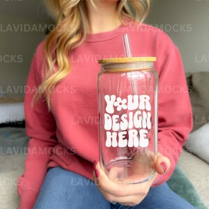May include: A person holding a clear glass tumbler with a bamboo lid and a straw. The tumbler has a white sticker that says "Your Design Here" in a retro font.