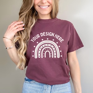 May include: A maroon t-shirt with a white graphic of a rainbow with hearts and dots. The text "YOUR DESIGN HERE" is above the rainbow.