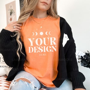 May include: A woman wearing a black cardigan with white ghost designs over a peach colored t-shirt with the text "YOUR DESIGN HERE" in white.
