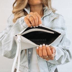 May include: A white leather clutch with a zipper closure and a long strap. The clutch is open and the inside is black.