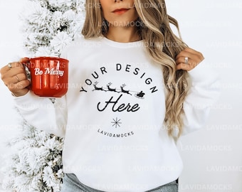 Könnte beinhalten: Weißer Pullover mit einem schwarzen Design eines Rentiers, das einen Schlitten zieht, mit dem Text "Your Design Here". Der Pullover wird von einer Person gehalten, die eine rote Tasse mit dem Text "Be Merry" hält.