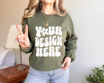 Puede incluir: Una sudadera verde con el texto "YOUR DESIGN HERE" en blanco, en letras estilizadas. La sudadera tiene cuello redondo y mangas largas.