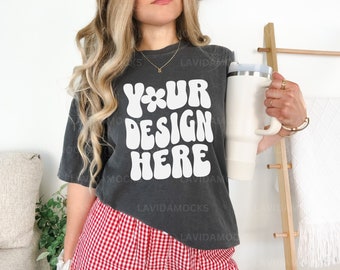 May include: A dark grey t-shirt with the text "Your Design Here" in white, featuring a retro, groovy font style. The shirt is being worn by a person with long blonde hair and a red and white gingham skirt.