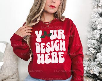 May include: A red sweatshirt with the text "YOUR DESIGN HERE" in white, with a holly and berry design. The sweatshirt is a mock-up, perfect for showcasing custom designs. The model is wearing the sweatshirt.