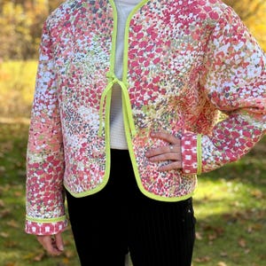 Può includere: Una giacca trapuntata con stampa floreale rosa e verde con bordino e chiusura a cravatta verde lime.