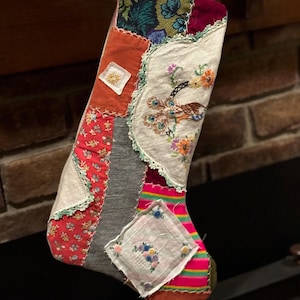 Può includere: Una calza di Natale patchwork con una varietà di tessuti. La calza presenta stampe floreali, dettagli ricamati e un motivo a pavone. La tavolozza dei colori comprende rosso, arancione, verde e grigio.