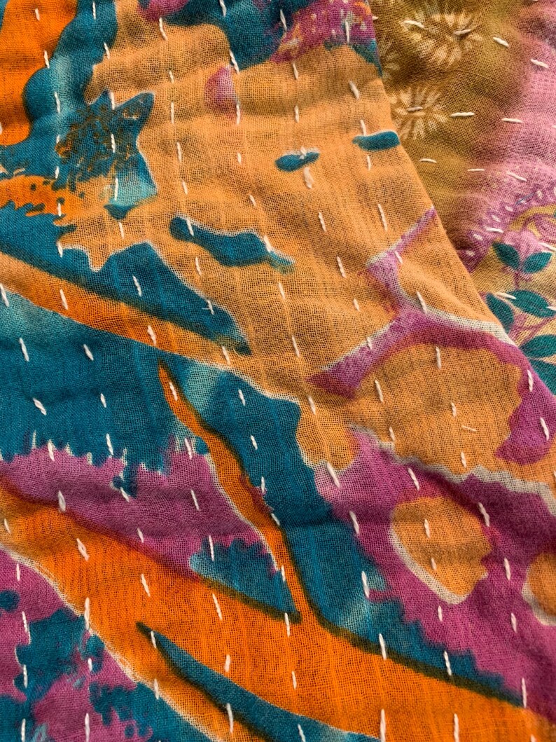 Puede incluir: Primer plano de un textil colorido con un dise&ntilde;o de patchwork. La tela presenta una vibrante mezcla de tonos turquesa, naranja y morado, con costuras blancas. El textil tiene un aspecto suave y texturizado.