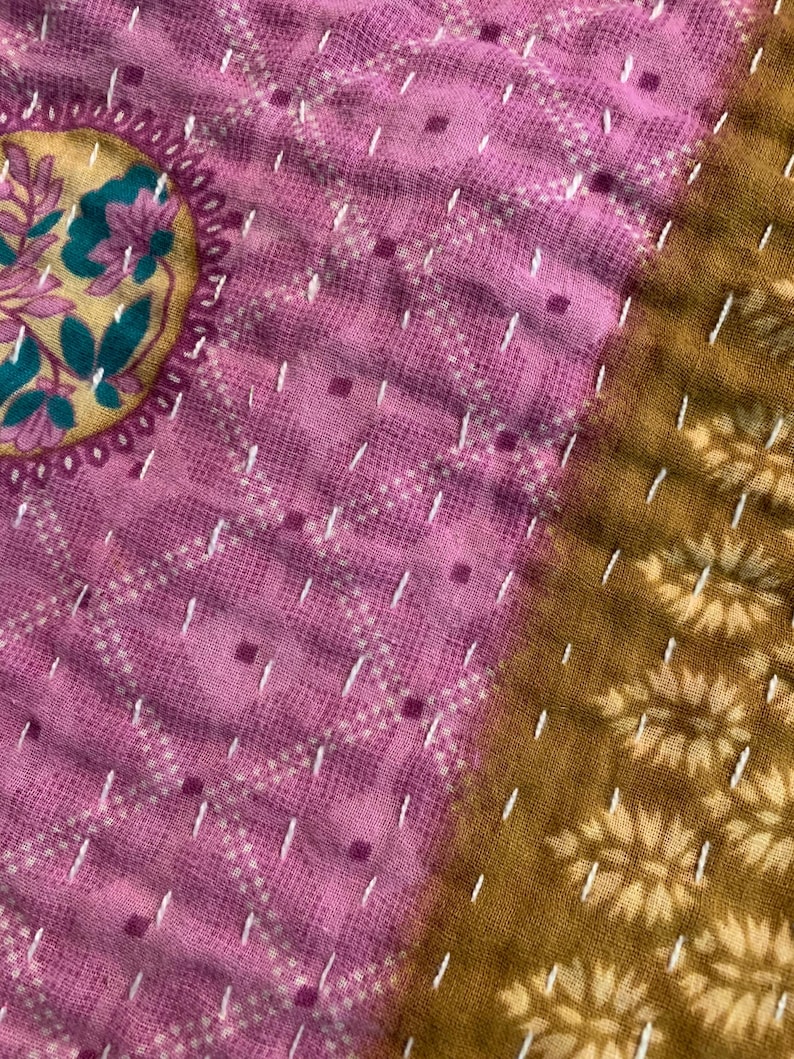 Puede incluir: Primer plano de una tela acolchada con un medall&oacute;n floral en oro, verde azulado y rosa. La tela presenta una combinaci&oacute;n de colores rosa y dorado con costuras blancas. El dise&ntilde;o incluye patrones geom&eacute;tricos y motivos florales.