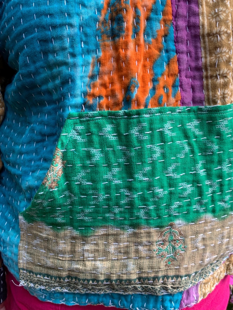 Puede incluir: Una chaqueta patchwork con una vibrante mezcla de colores y texturas. La chaqueta presenta un patr&oacute;n te&ntilde;ido anudado en azul turquesa y naranja, un bolsillo verde y secciones a rayas marrones y moradas. Costuras blancas detallan las costuras.