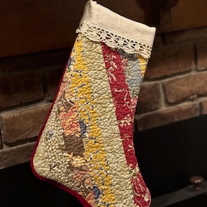 Può includere: Una calza natalizia trapuntata con pannelli diagonali in tessuto floreale nei toni del giallo, rosso e blu tenue. Il risvolto superiore è in tessuto beige tinta unita con bordo in pizzo bianco e un occhiello in tessuto per appenderla.