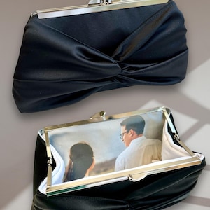 May include: A black satin clutch with a silver clasp. The clutch has a photo insert that shows a couple in a landscape setting.