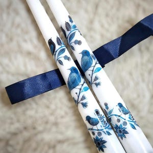 Puede incluir: Dos velas de té blancas con diseños de pájaros azules y negros y flores.