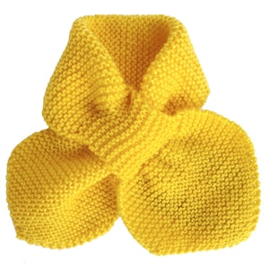 May include: A bright yellow knitted scarf, displayed against a white background. The scarf is made of a thick yarn, with a textured, ribbed appearance. The scarf is folded over itself, creating a loop and two rounded ends.