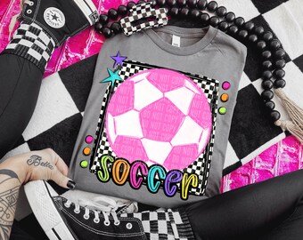 May include: A gray t-shirt with a pink soccer ball graphic and the word "Soccer" in colorful letters. The soccer ball is on a black and white checkered background.