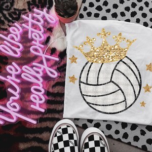 May include: White t-shirt with a gold glitter crown and a volleyball with a gold glitter outline. The text "You're like really pretty" is on a pink neon sign in the background.