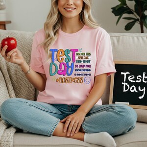 Könnte beinhalten: Ein hellrosa T-Shirt mit den Worten "Test Day" in bunten Buchstaben. Das Shirt zeigt auch die Sätze "You got this, Stay cool, Think smart, Do your best, You're prepared, No big if's, und No Stress" mit einem Smiley.