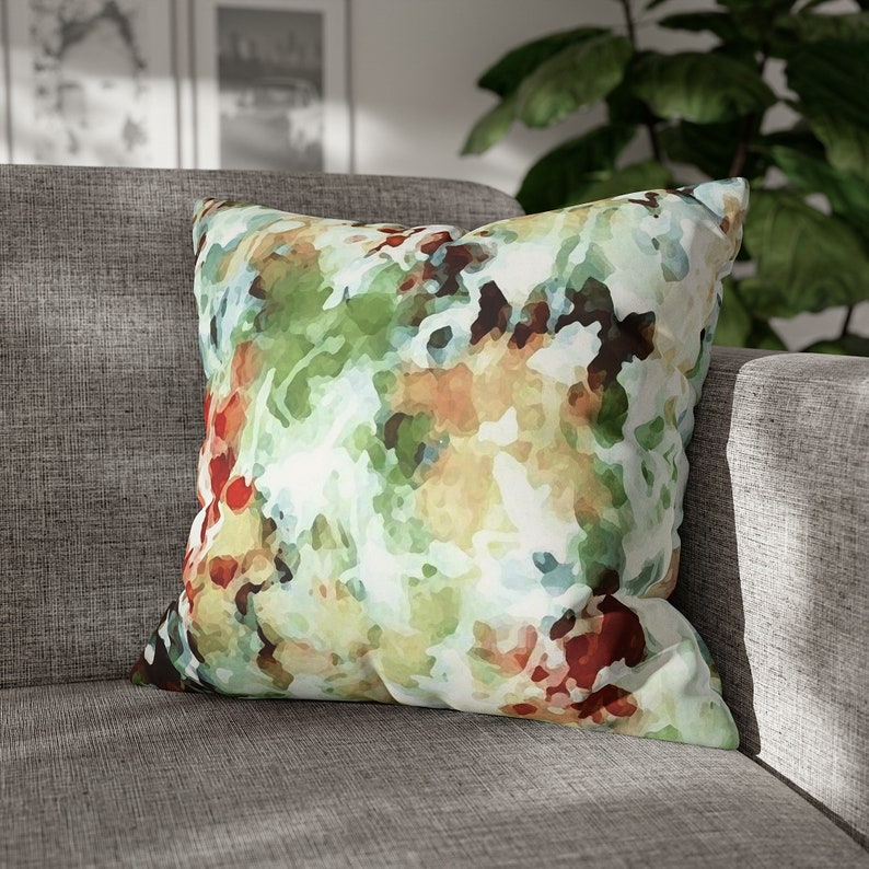 This image shows a square throw pillow with an abstract floral design. The modern impressionist design features brushstrokes of green, brown, & red watercolor paint resembling branches, leaves, & petals.